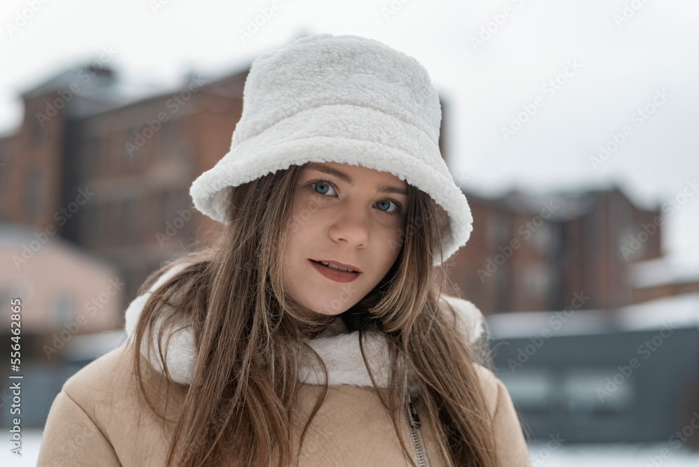 Portrait of young smiling woman in fashionable white fur panama in winter outdoors. Girl in trendy headdress Portrait of young smiling woman in fashionable white fur panama in winter outdoors. Girl in trendy headdress
