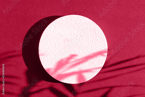 Abstract minimal scene of a geometrical form. A cylindrical white podium on a magenta background with a shadow of tropical palm leaves. Scene to show cosmetic podructs. Showcase, display case.