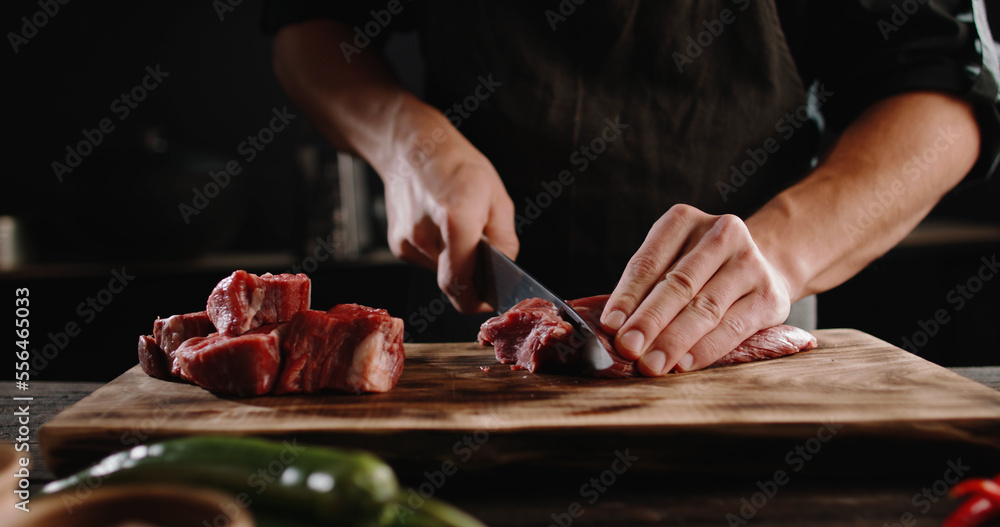 Chef sharpening his knife in front of raw piece of steak. Cooker preparing his tools for cutting meat for grilling on professional kitchen table