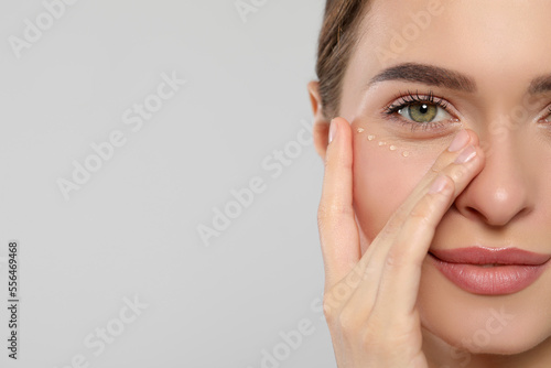 Young woman with cream around eye on white background, closeup. Space for text