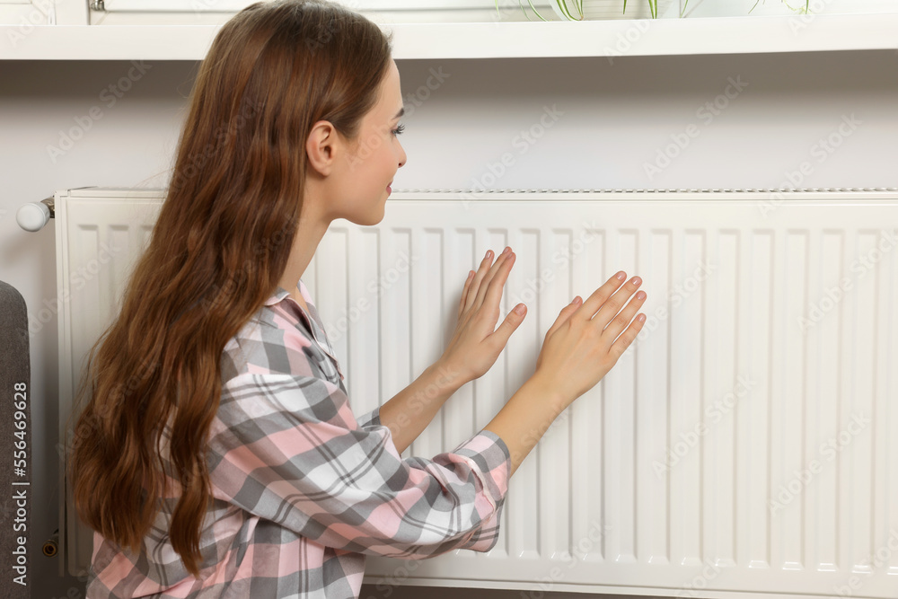 Woman warming hands on heating radiator near white wall Woman warming hands on heating radiator near white wall