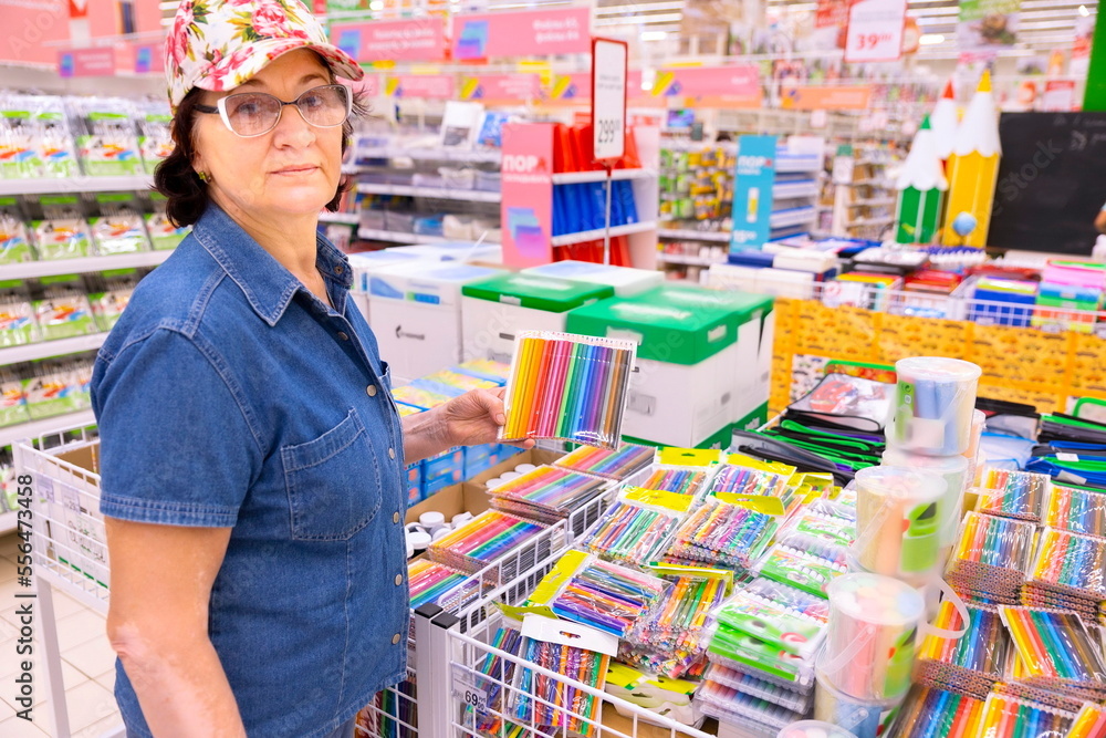 beautiful mature women holding a set of colored pencils in the stationery department in a large supermarket