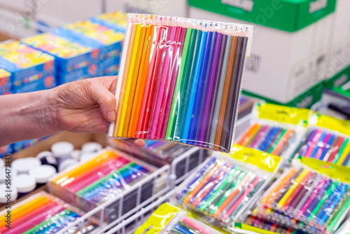a woman's hand holds a large pack of colored pencils in the stationery department of a supermarket