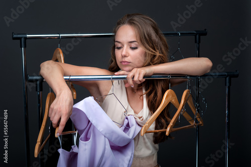 A beautiful girl leaning on a rack of clothes, deciding what clothes to choose. Isolated on dark background