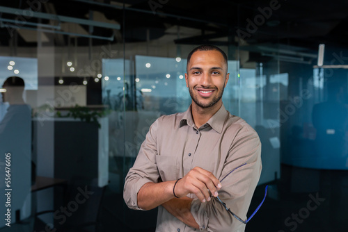 Portrait of african american businessman in office, man in shirt standing near window smiling and looking at camera, programmer working inside development company.