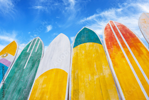 Canvas Print Several surfboards of different colorful saturated yellow, green, red colors lined up against the background of a blue summer sky with clouds at sunny day