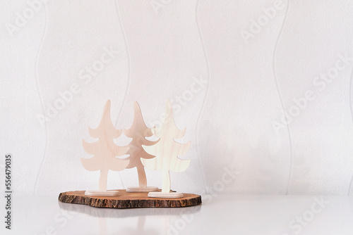 Christmas interior decor. Three toy Christmas trees made of plywood on tree cut, white wall. © IrinaK