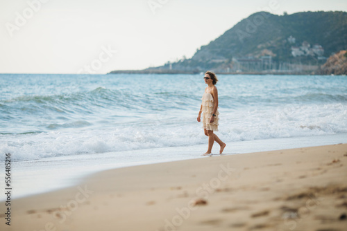 The girl walks along the shore along the sea at sunset.