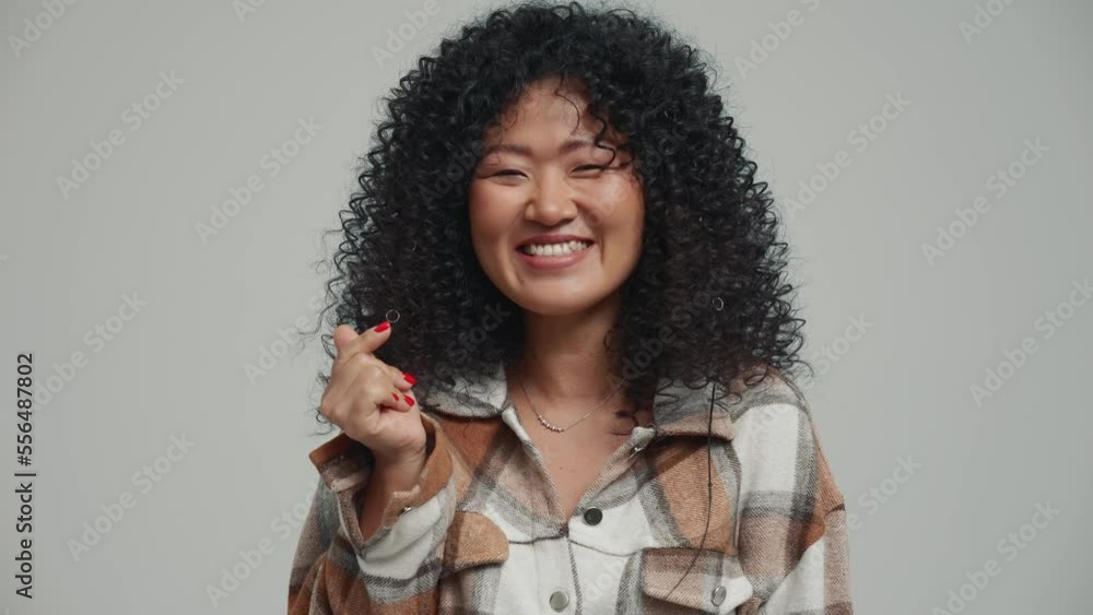 Lovely brunette Asian woman showing Korean heart shape gesture at the camera in the grey studio Lovely brunette Asian woman showing Korean heart shape gesture at the camera in the grey studio