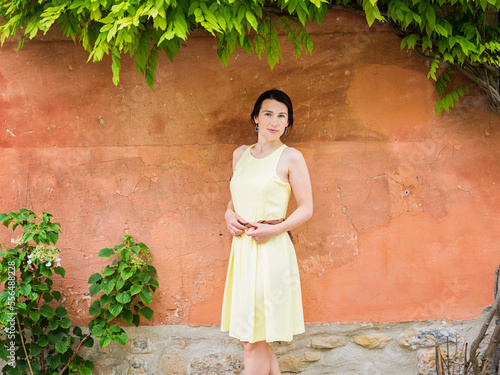 Lifestyle portrait of young stylish woman staying on the street in old town nead orange wall, wearing yellow dress photo