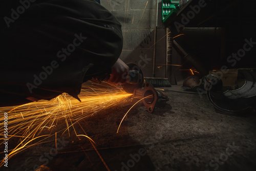 Pipe cutting, sparks fly. Car service. On the ground in a pit. Man repairing of corrugation muffler catalyst of exhaust system in car workshop - mechanic cleans the muffler pipe by angle grinder