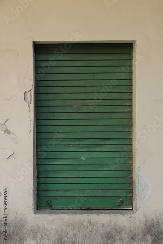 green window with shutters, Stone wall with window and green roll up metal jalousie, vertical format