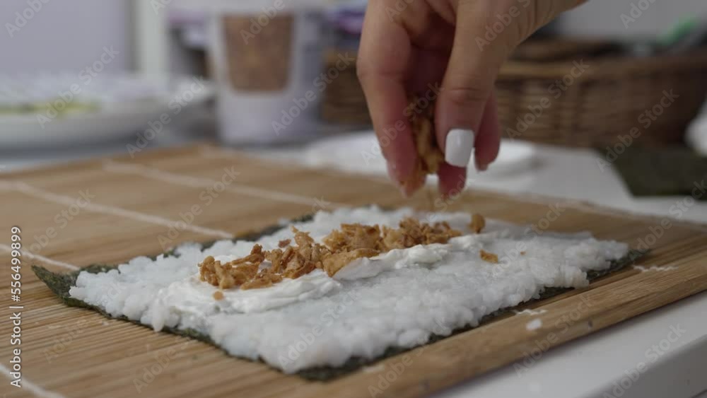 Video of an unrecognizable woman's hand pouring crispy onion on top of cheese spread on a sheet of nori seaweed for ready to make homemade sushi at her kitchen table. Video of an unrecognizable woman's hand pouring crispy onion on top of cheese spread on a sheet of nori seaweed for ready to make homemade sushi at her kitchen table.