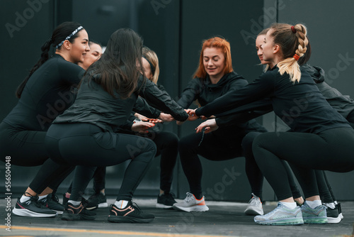 Conception of teamwork. Group of sportive women is outdoors near black building