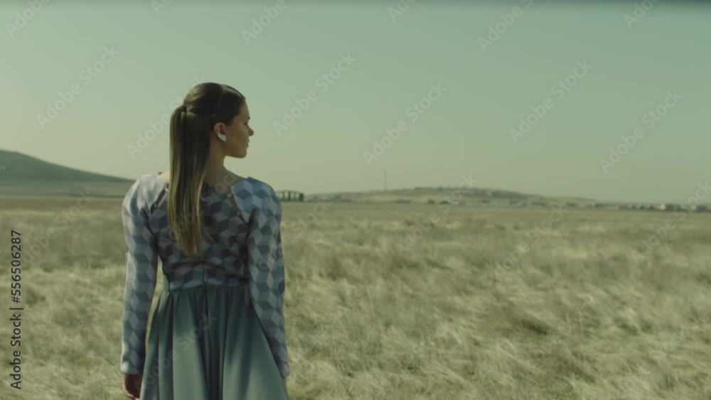 Rear view of woman walking in slow motion through a field . Young stylish lonely girl walking on meadow field . Long skirt fabric flowing by wind . Fashion style . Shot on ARRI Alexa Cinema Camera Rear view of woman walking in slow motion through a field . Young stylish lonely girl walking on meadow field . Long skirt fabric flowing by wind . Fashion style . Shot on ARRI Alexa Cinema Camera