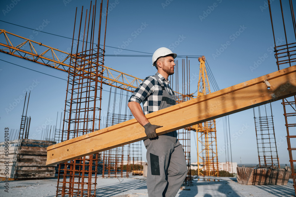 Moving wooden plank. Man is working on the construction site at daytime