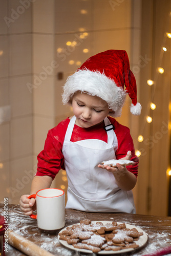 Christmas. Adorable little boy eating Christmas cookies and drinking hot tea in the New Year's decorations. Winter holidays.