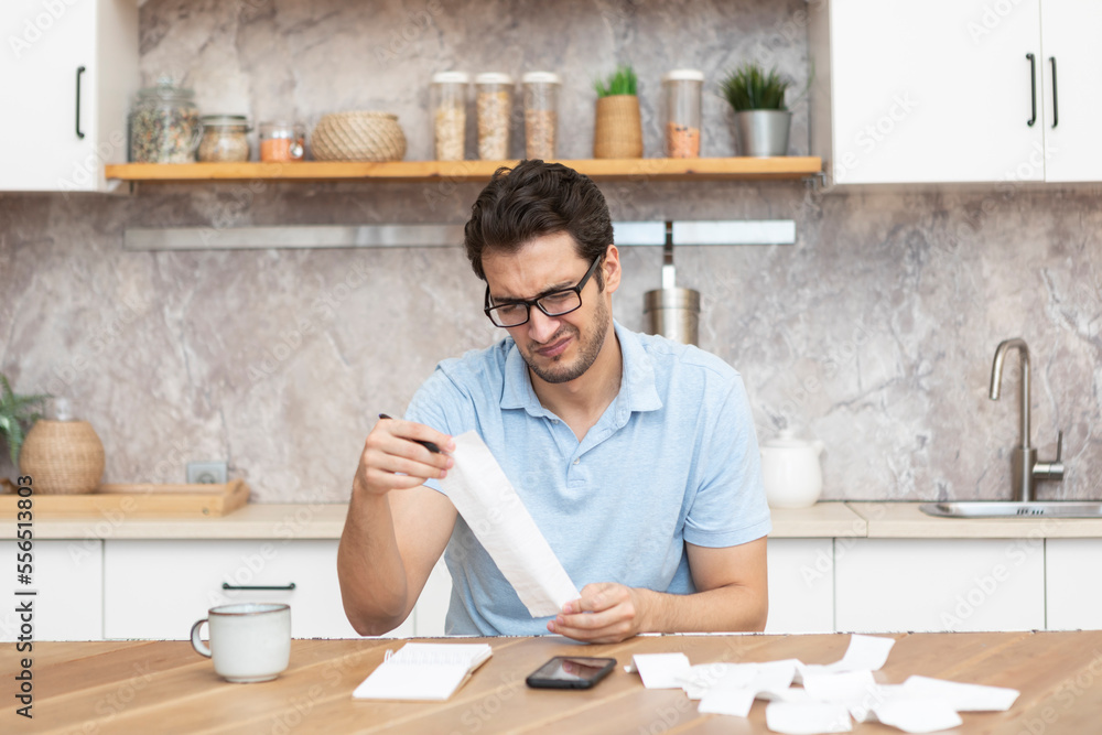 Close up of unhappy man sitting at the table, stressed and confused by calculate expense from invoice or bills, have no money to pay mortgage or loan. High prices and spending money concept Close up of unhappy man sitting at the table, stressed and confused by calculate expense from invoice or bills, have no money to pay mortgage or loan. High prices and spending money concept