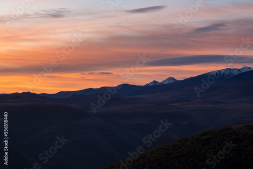 Dark silhouettes of mountains against a bright orange sunset sky. Red sunset over majestic mountains. Sunset in magenta tones. Atmospheric purple landscape with a high-altitude snowy mountain valley.