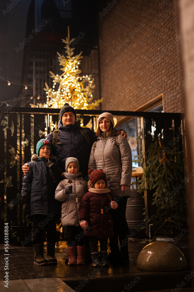 Family stand against illuminated Christmas tree outdoor in evening.