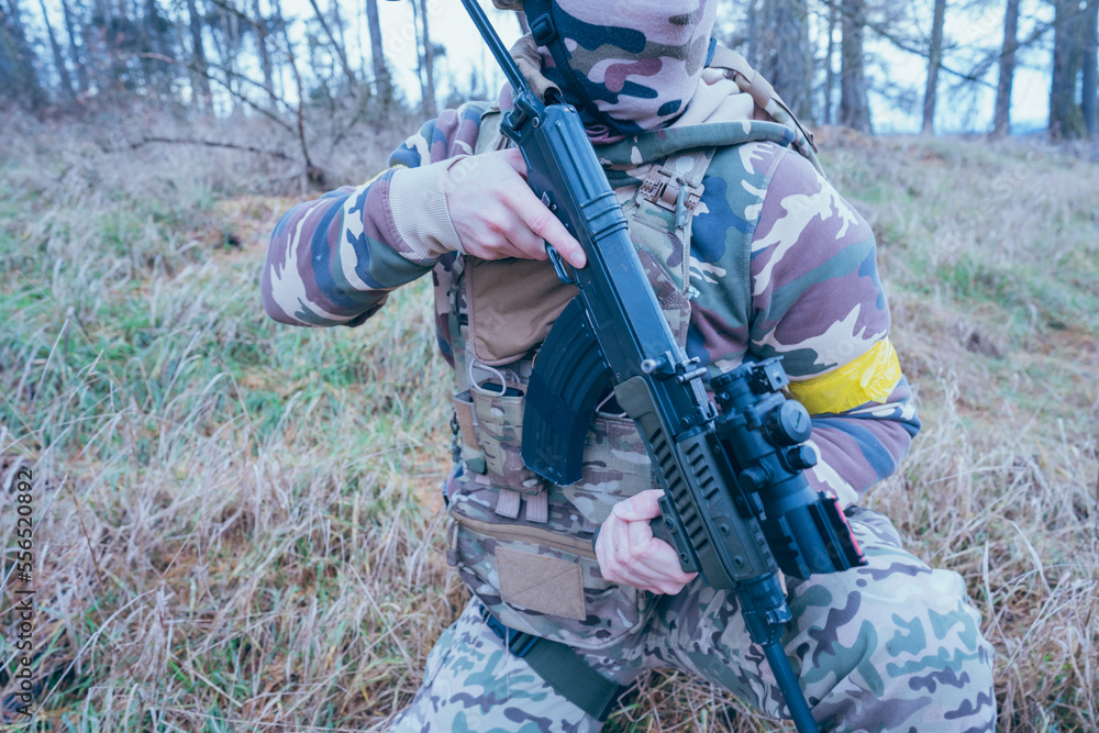 Fototapeta premium Ukrainian soldier on the front line. With an assault rifle in camouflage. Yellow tape. 