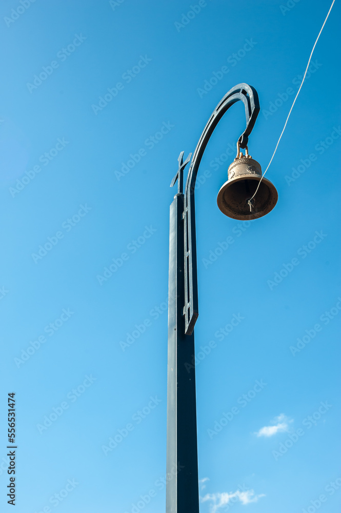a Christian Church bell against a blue sky, standing on a separate support and with a rope to ring the bell. a Christian Church bell against a blue sky, standing on a separate support and with a rope to ring the bell.