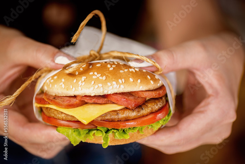 Hands holding a delicious burger with grilled meat, tomato and cheese. Hambuguer with salada, cheese anda saudage photo