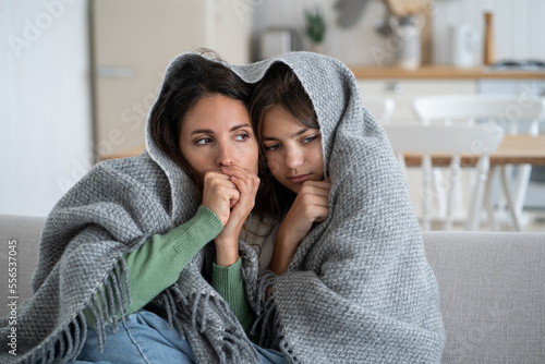 Vászonkép Unhappy frozen woman with daughter are sits on couch cuddling up to each other wrapped in warm blanket