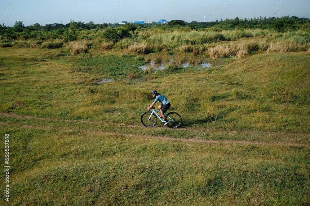 Obraz premium A young bearded cyclist is biking through a field