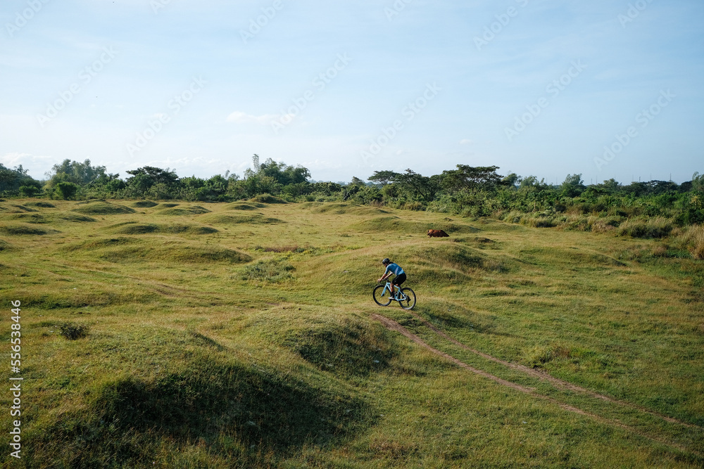 A young bearded cyclist is biking through a field A young bearded cyclist is biking through a field