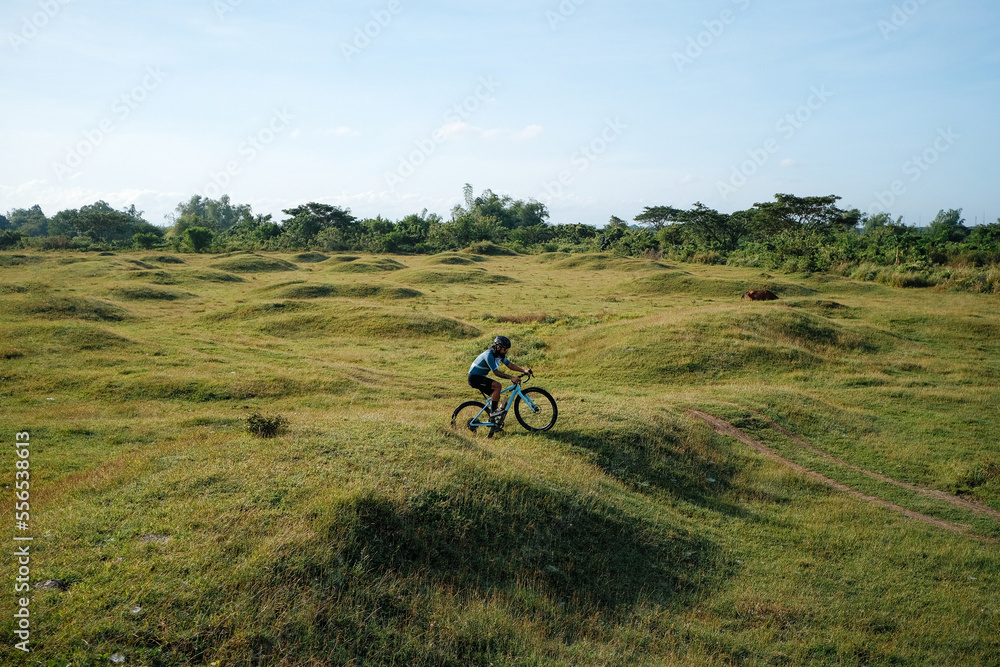 A young bearded cyclist is biking through a field