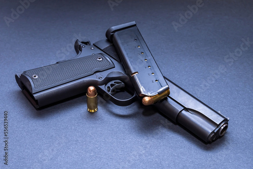 A 45 caliber 1911 model pistol with a loaded magazine on top of it and another bullet next to it with a dark background photo