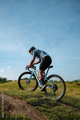 A young bearded cyclist is biking through a field