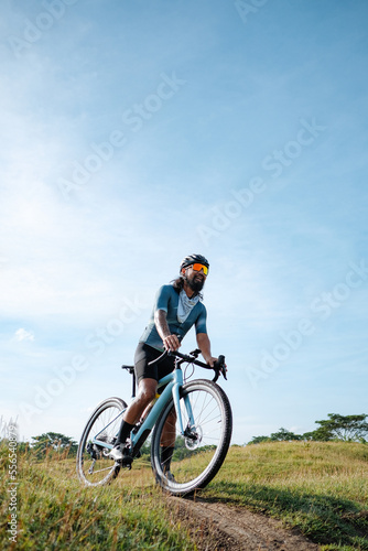 A young bearded cyclist is biking through a field