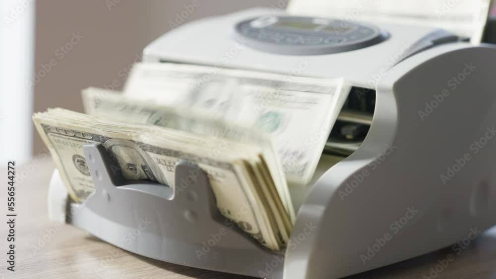 Male Caucasian hand pressing start button and hundred banknotes counting in device. Unrecognizable man calculating income with machine indoors on table. Banking concept Male Caucasian hand pressing start button and hundred banknotes counting in device. Unrecognizable man calculating income with machine indoors on table. Banking concept