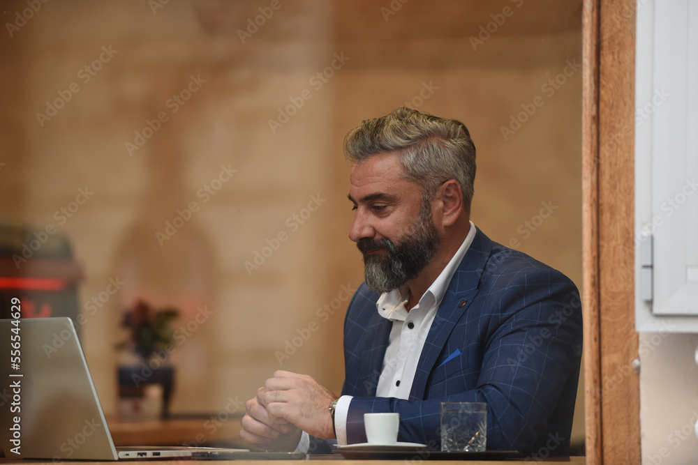 Fototapeta premium Modern senior businessman sitting in cafe and using laptop and smartphone