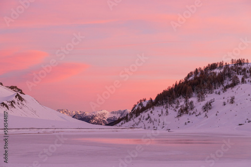 Luci rosse al crepuscolo. Sulle bianche distese di neve si specchiano i colori del cielo del crepuscolo in alta montagna al confine tra Italia e Francia photo