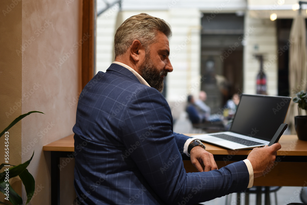Modern senior businessman sitting in cafe and using laptop and smartphone Modern senior businessman sitting in cafe and using laptop and smartphone
