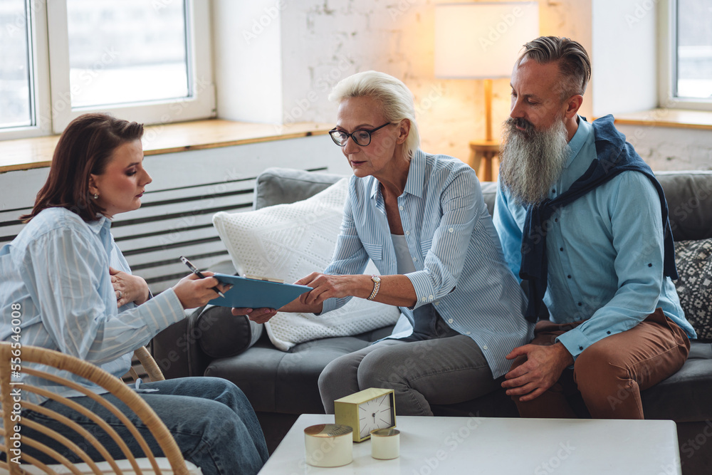Senior couple, mature man and woman, husband and wife sitting on the sofa on the therapy session at psychologist cabinet, discussing stress, family problems. Concept of mental health care Senior couple, mature man and woman, husband and wife sitting on the sofa on the therapy session at psychologist cabinet, discussing stress, family problems. Concept of mental health care