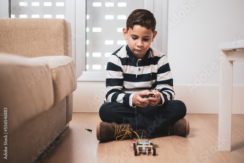 A boy sitting on the floor of his house while playing with a car with a solar panel. Science games. photo