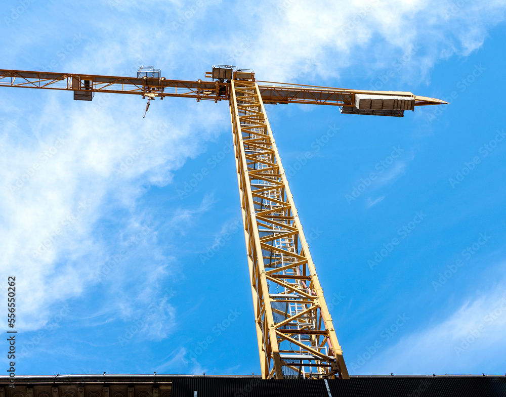Yellow tower crane in a construction site. On the background, bright blue sky with few clouds. Yellow tower crane in a construction site. On the background, bright blue sky with few clouds.