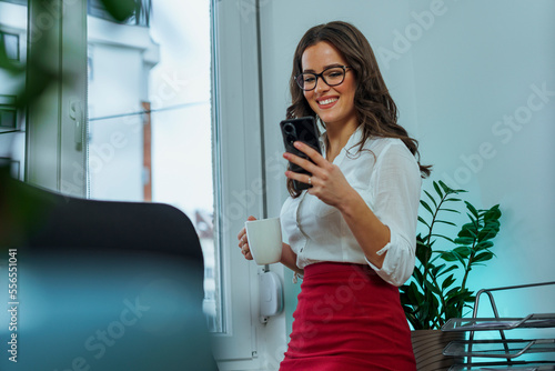 Business woman is scrolling on her phones and smiles at a funny video as she drinks coffee on her break