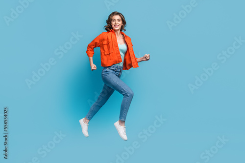 Full body photo of young lovely lady flying running fast hurry sale shopping wear trendy orange outfit isolated on blue color background