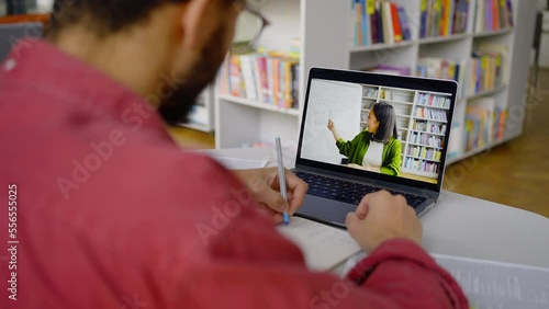 Focus on laptop monitor streaming online lesson. Blurred student taking notes on the foreground photo