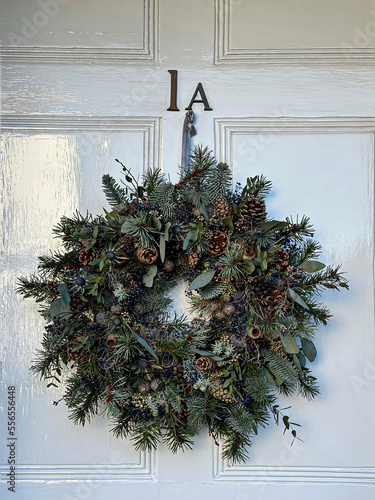 Christmas wreath on a wooden door. Christmas mood. Elegant christmas wreath decorated oranges, pine cones and lotus on a white wooden door. Beautiful vintage door. estive christmasy themed winter natu