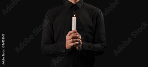 Jewish man with burning candle honoring victims of Holocaust on dark background
