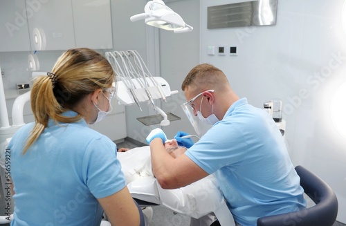doctor in blue gloves applies an ointment to patient s teeth that shows where is plaque that needs to be cleaned. getting teeth cleaning and polishing at clinic Dentist working on patient in chair