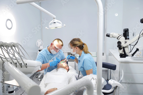 doctor in blue gloves applies an ointment to patient's teeth that shows where is plaque that needs to be cleaned. getting teeth cleaning and polishing at clinic Dentist working on patient in chair