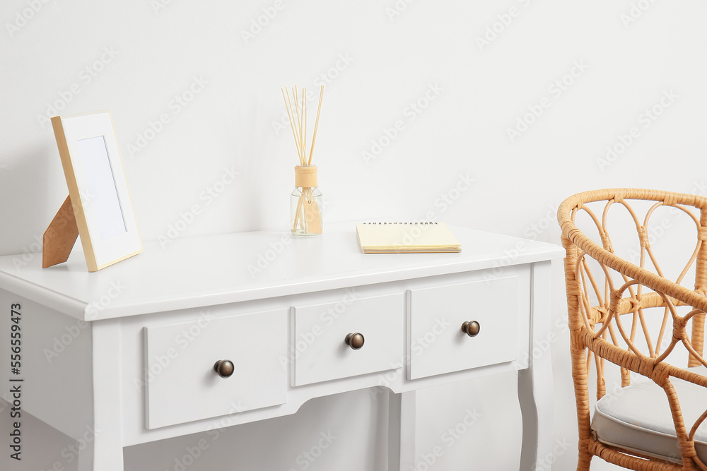 Blank photo frame, reed diffuser and notebook on table near white wall