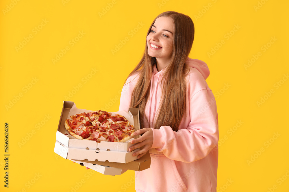 Beautiful young woman holding boxes with fresh pizza on yellow background